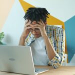 Frustrated man at laptop desk experiencing chrome browser freezing during a work presentation