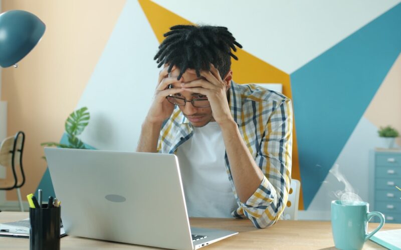 Frustrated man at laptop desk experiencing chrome browser freezing during a work presentation