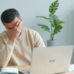Frustrated man rubbing his face in front of a laptop after losing a password puzzle game
