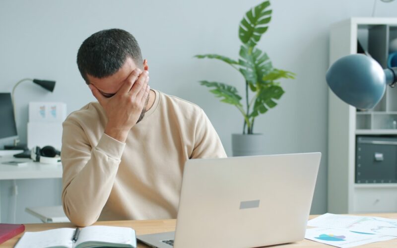 Frustrated man rubbing his face in front of a laptop after losing a password puzzle game