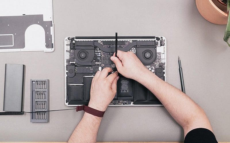 Technician using a screwdriver to repair a laptop on a workbench during a virus removal service