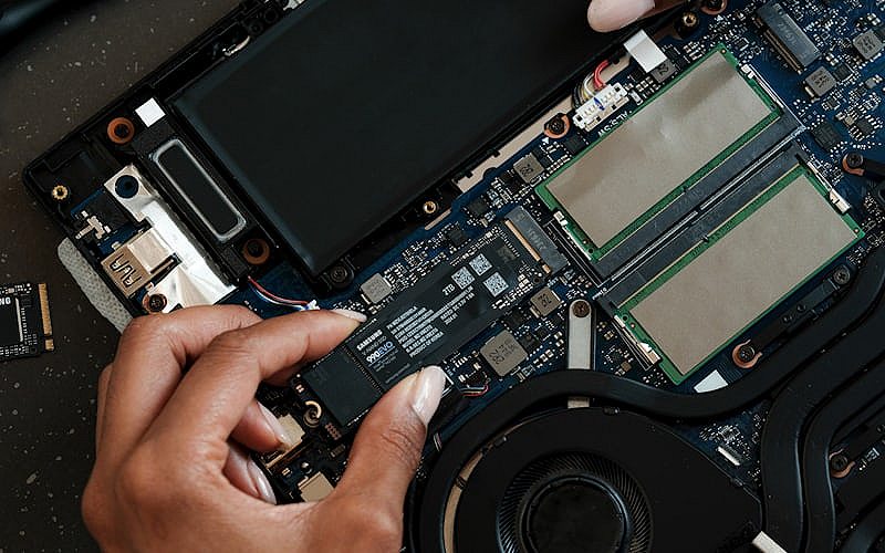 Close-up of a person repairing a laptop motherboard with precision tools during hardware diagnostics